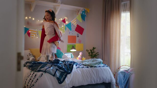 happy little girl jumping on bed wearing costume playing game enjoying playful imagination in colorful bedroom at home