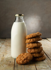 A bottle of milk and a stack of cookies on a wooden table.