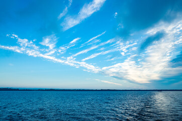 River landscape. Calm water and beautiful blue sky with clouds. Trees grow on the nearest shore. There is copy space