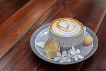 A cup of cappuccino with bitcoin on wooden table at cafe. Cryptocurrency trading concept