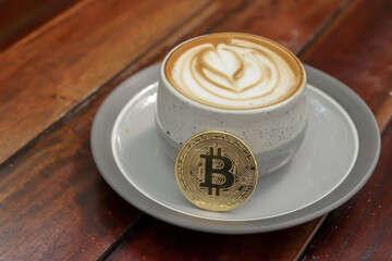 A cup of cappuccino with bitcoin on wooden table at cafe. Cryptocurrency trading concept
