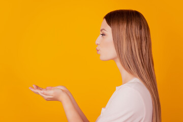 Profile portrait of sweet tempting blone lady look empty space hold palms blow air kiss on yellow background