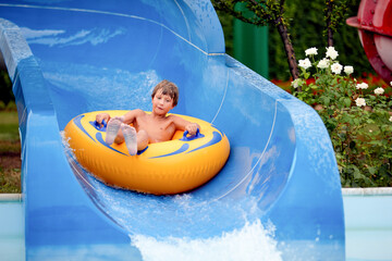 happy an 8 year old boy is riding in the water Park on inflatable circles on water slides with...
