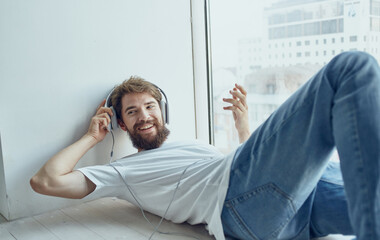 young man lying near the window wearing headphones technology