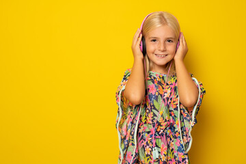 Cute little girl in headphones listening music isolated over yellow background.