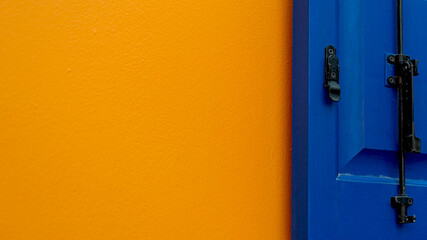 Deeep blue wooden window shutter on bright orange and white wall, color compbination in outdoor architecture design