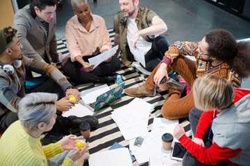 Team sitting on office floor, discussing paperwork