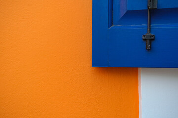 Deeep blue wooden window shutter on bright orange and white wall, color compbination in outdoor architecture design