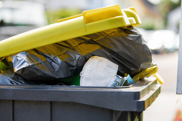 full garbage trash can with ffp2 face mask standing at sidewalk waiting to get empty the recyclable...