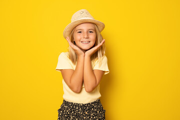 Portrait of cute smiling little girl wearing straw hat isolated over yellow background.