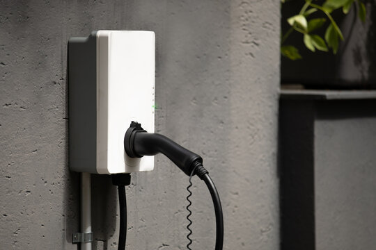 plug holder for wall mount charging station with cable at wall box mounted to concrete house wall ready to load and tank electrical cars with power instead of gasoline to be an alternative way of fuel