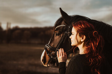 2 heads one love! stallion with head collar and redhead woman are bonding while being intimate...