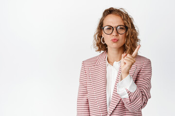 Obraz na płótnie Canvas Bossy business woman in glasses scolding someone, shaking finger in disapproval, boss around, standing over white background