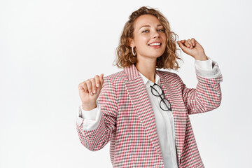 Dancing female entrepreneur smiling, having fun and relaxing, standing in suit against white background