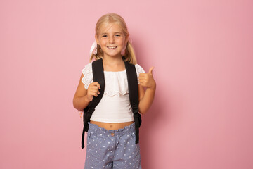 Little schoolgirl show thumb up isolated over pink background - obrazy, fototapety, plakaty