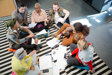 Team sitting on office floor, discussing paperwork
