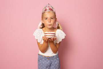 Cute little girl with princes crone and holding a cake isolated over pink background. Celebration...