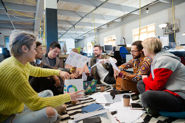 Team sitting on office floor, discussing paperwork