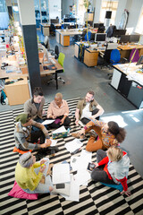 Team sitting on office floor, discussing paperwork