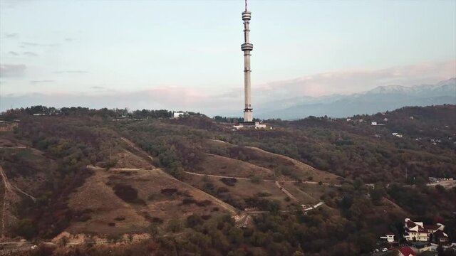 Red orange sunset against the TV tower. Visible clouds, the sun sets over the horizon. Around the green trees, mountains and high tower. Shooting with the drone. Beautiful panorama. Almaty city,