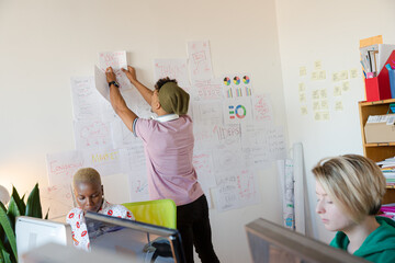 Young man hanging work plan schedule on wall in office