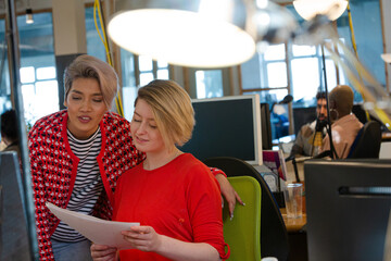 Young women discussing paperwork at computer