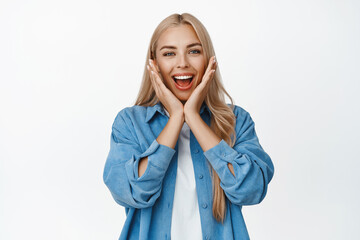 Super happy girl rejoicing, holding hands near face and smiling surprised, receive big good news, standing over white background