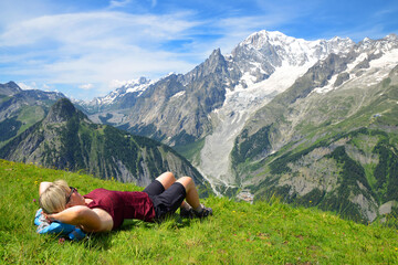 Fototapeta na wymiar Tourist lying on a meadow in sunny day, at the background Mont Blanc ( Monte Bianco ) mountain range. Aosta valley, Italy.