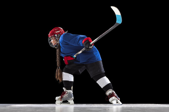 Full-length portrait of child girl, hockey player isolated over black background. Side view