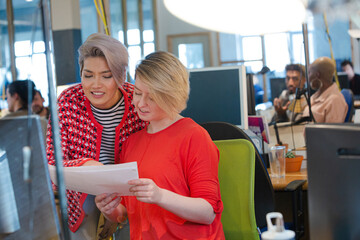 Young women discussing paperwork at computer