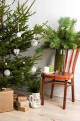 Christmas tree with white toys, old chair with a vase with pine branches, gift boxes under the tree, part of home interior