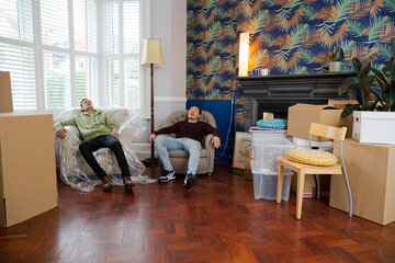 Men taking a break from moving house, relaxing and laughing in armchairs