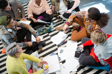 Team sitting on office floor, discussing paperwork