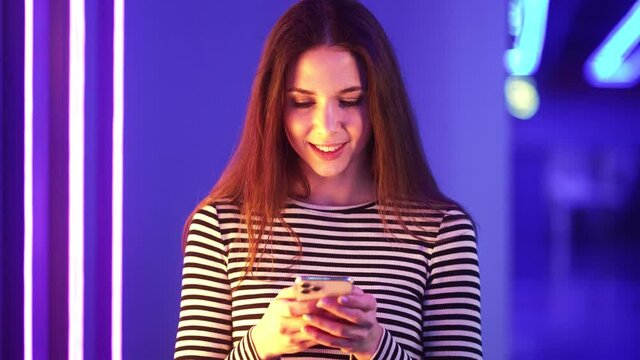 Positive woman using her phone standing in the neon blue hall