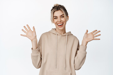 Happy smiling woman showing empty raised hands, laughing and looking carefree at camera, standing in casual clothes over white background