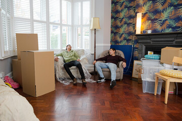 Men taking a break from moving house, relaxing and laughing in armchairs