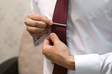 The groom adjusts the clip on the burgundy tie packing for the wedding.