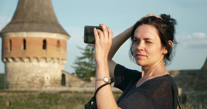 Female Tourist Takes Pictures Photo Shoots on Smartphone of Old Medieval Castle Fortress. Woman Travel Visit Sightseeing. Kamianets-Podilskyi Ukraine Europe. Summer Evening 4K