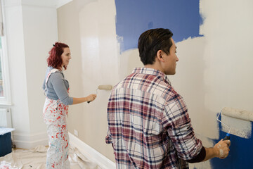 Happy, playful couple with paint rollers painting room