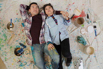 Happy couple relaxing, taking a break from painting, laying on dropcloth among paint cans