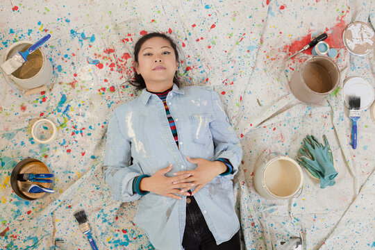 Woman Taking A Break From Painting, Laying On Dropcloth Among Paint Cans