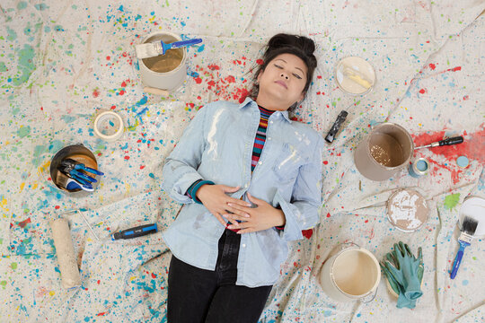 Woman Taking A Break From Painting, Laying On Dropcloth Among Paint Cans