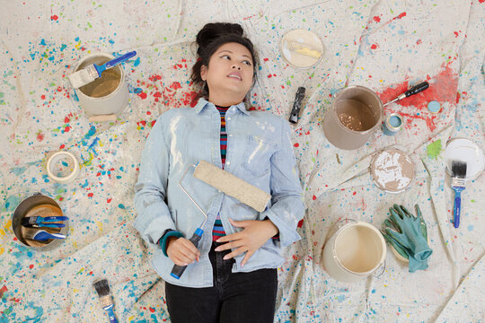 Woman Taking A Break From Painting, Laying On Dropcloth Among Paint Cans