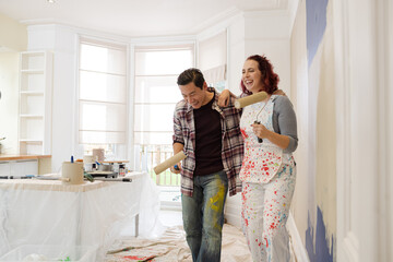 Happy, playful couple with paint rollers painting room