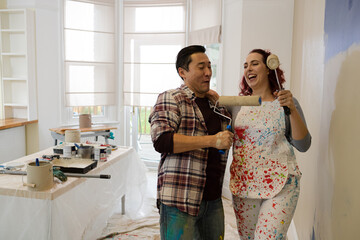 Happy, playful couple with paint rollers painting room