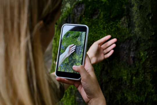 Girl holds a mobile phone in her hands and takes pictures of nature in the park to share photos on social networks. Focus on the phone screen. Make memories using your smartphone. Mobile phone closeup