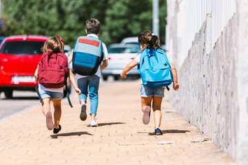 Unrecognizable schoolchildren in hurry running on sidewalk in city