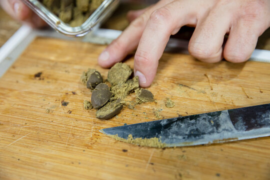 Crop man crushing dry marijuana piece on chopping board