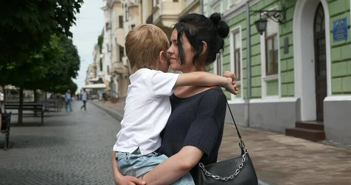 Happy Loving Mother Holds Son in Hands Embrace Hugging Looking Around. Woman Talk to Child Standing Among Street. Historic European Architecture City Downtown. Chernivtsi Ukraine Europe 4K