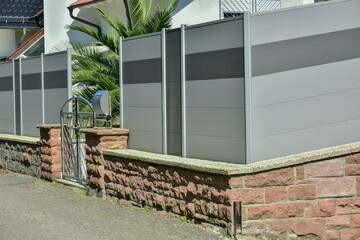 Natursteinmauer, Edelstahl-Gartentor und fest stehende Kunststoff-Sichtschutzwand und rot...